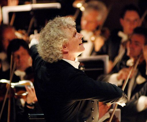 Conductor Sir Simon Rattle in action, leading an orchestra with passion.